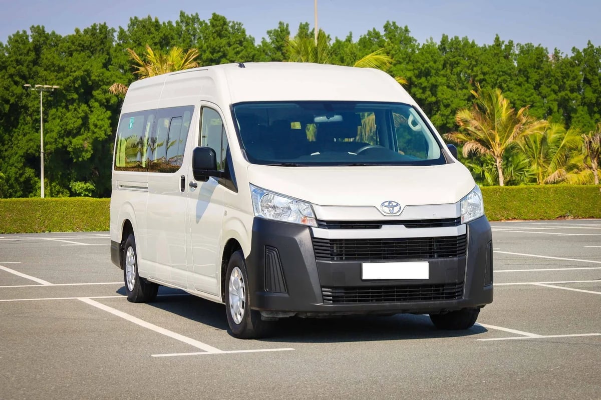 White Toyota minivan parked in an empty lot with green trees and grass in the background